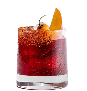 A deep red cocktail in a short glass garnished with tajin, mango, and a habañero