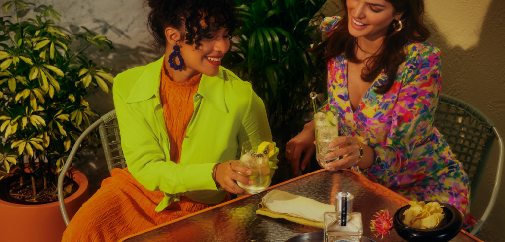 Two colorfully-dressed friends enjoy cocktails