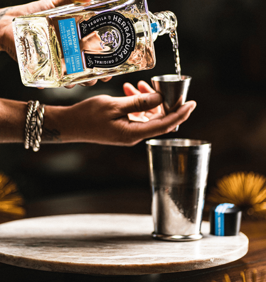 A person pouring a bottle of Herradura Silver