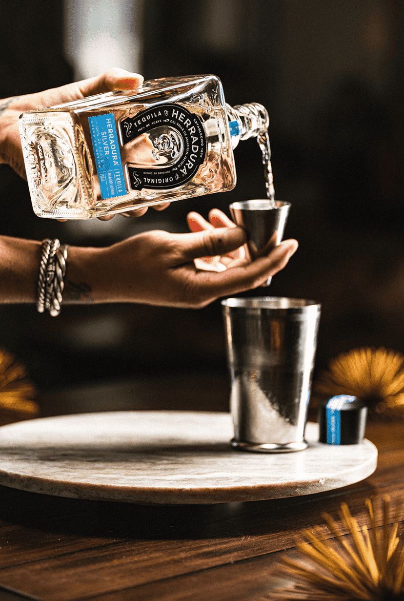 A person pouring a bottle of Herradura Silver